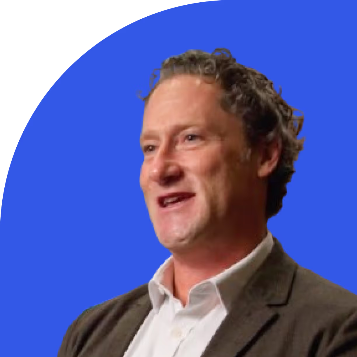 Man with curly hair wearing a white shirt and brown blazer against a blue circular background.